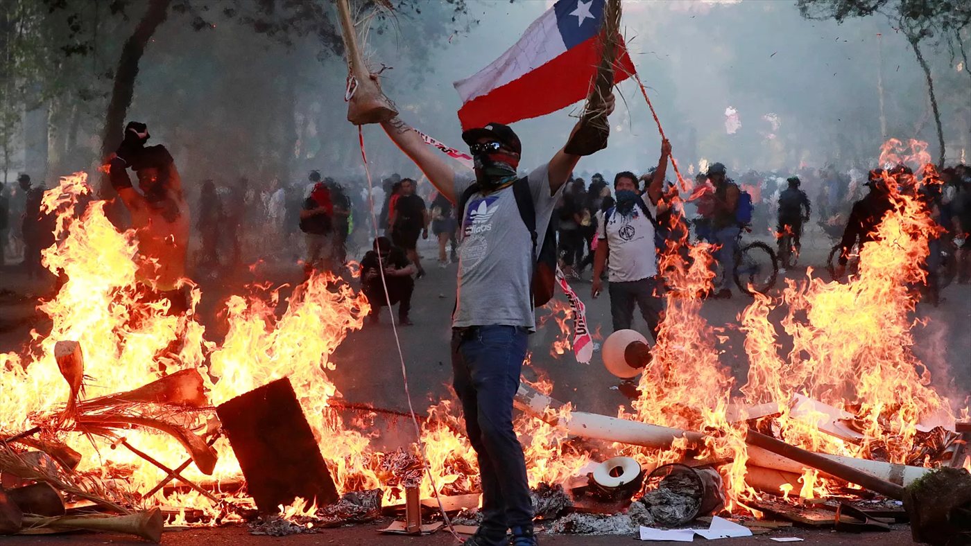 Manifestante con la bandera chilena entre barricadas encendidas, octubre de 2019