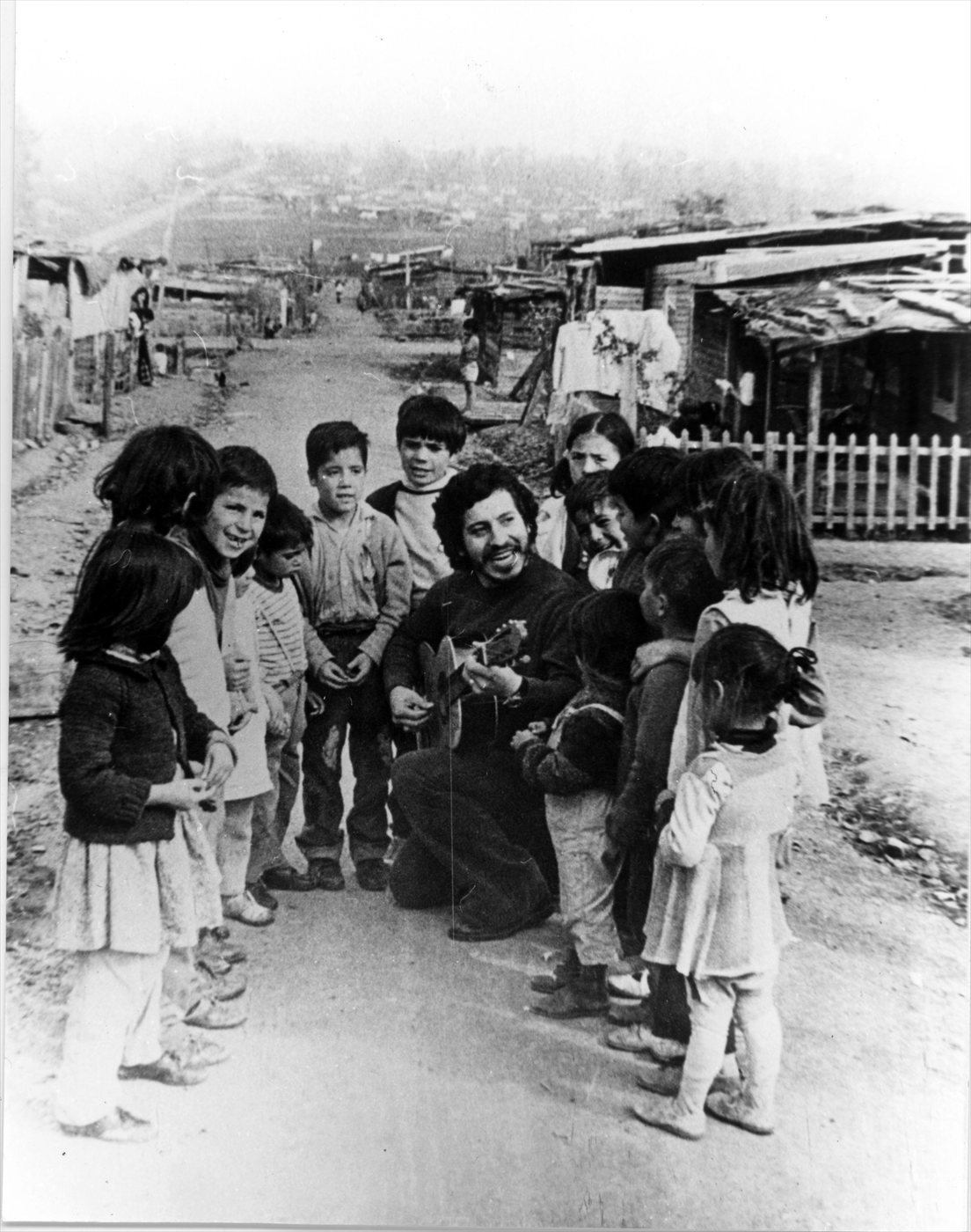 Víctor Jara cantando con su guitarra rodeado de niños en una población