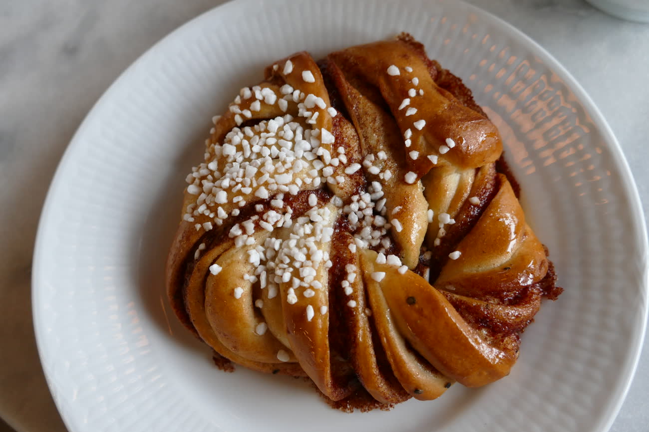 Un kanelbulle sueco con azúcar perlado, servido en un plato blanco