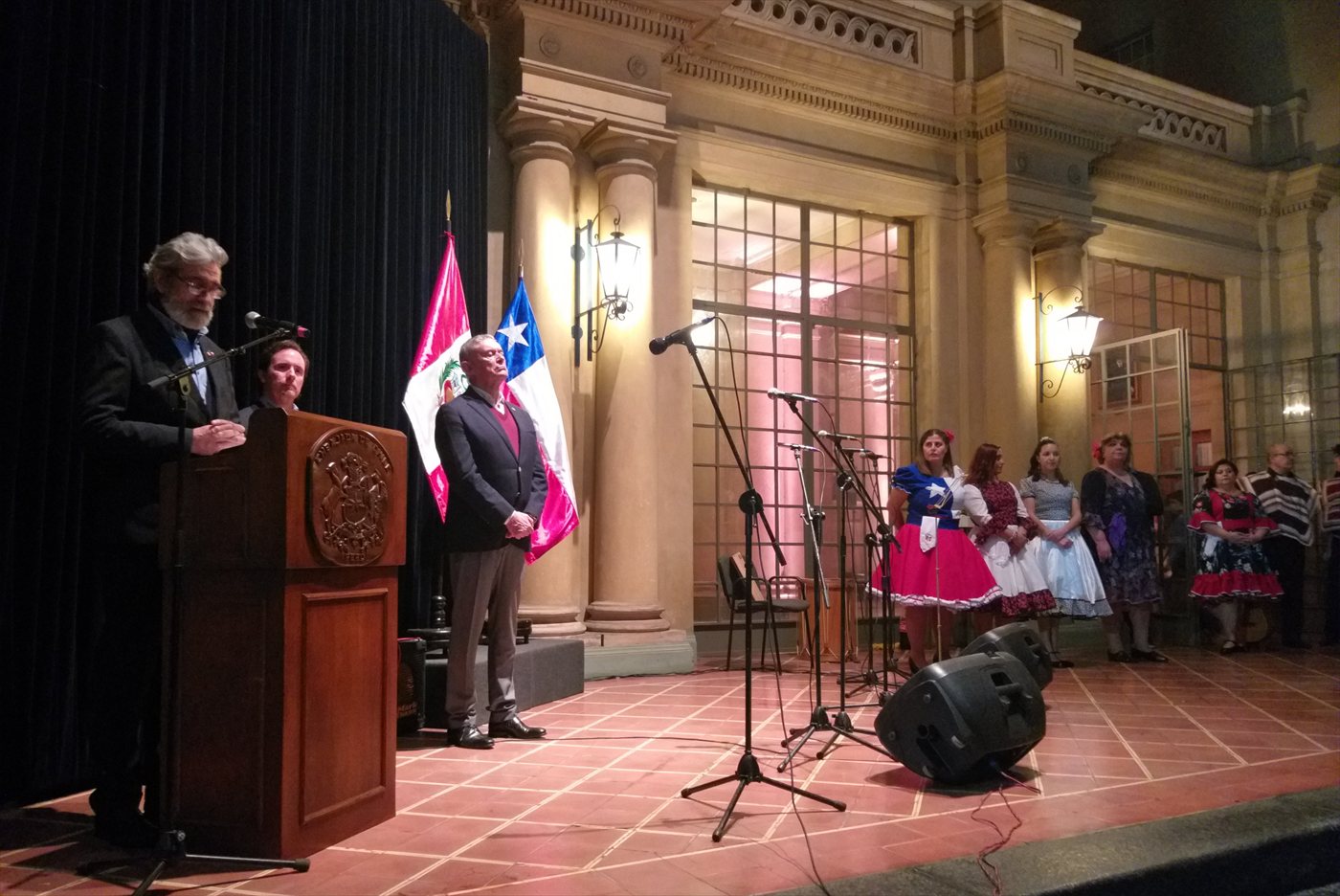 Acto de Fiestas Patrias en el extranjero, con las banderas de Perú y Chile y bailarinas de cueca en el escenario